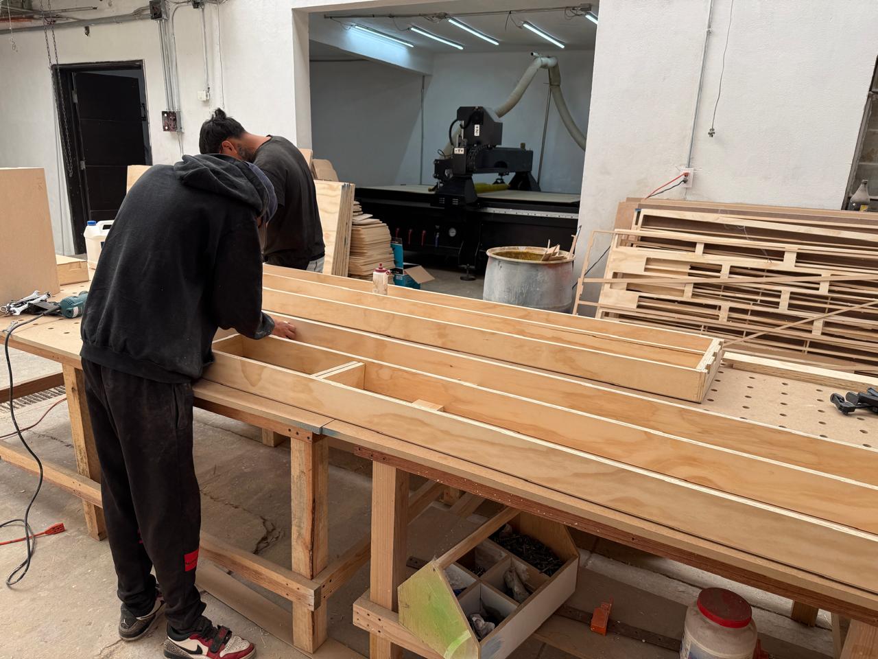 Verificación de piezas de triplay en el taller, con el router CNC al fondo